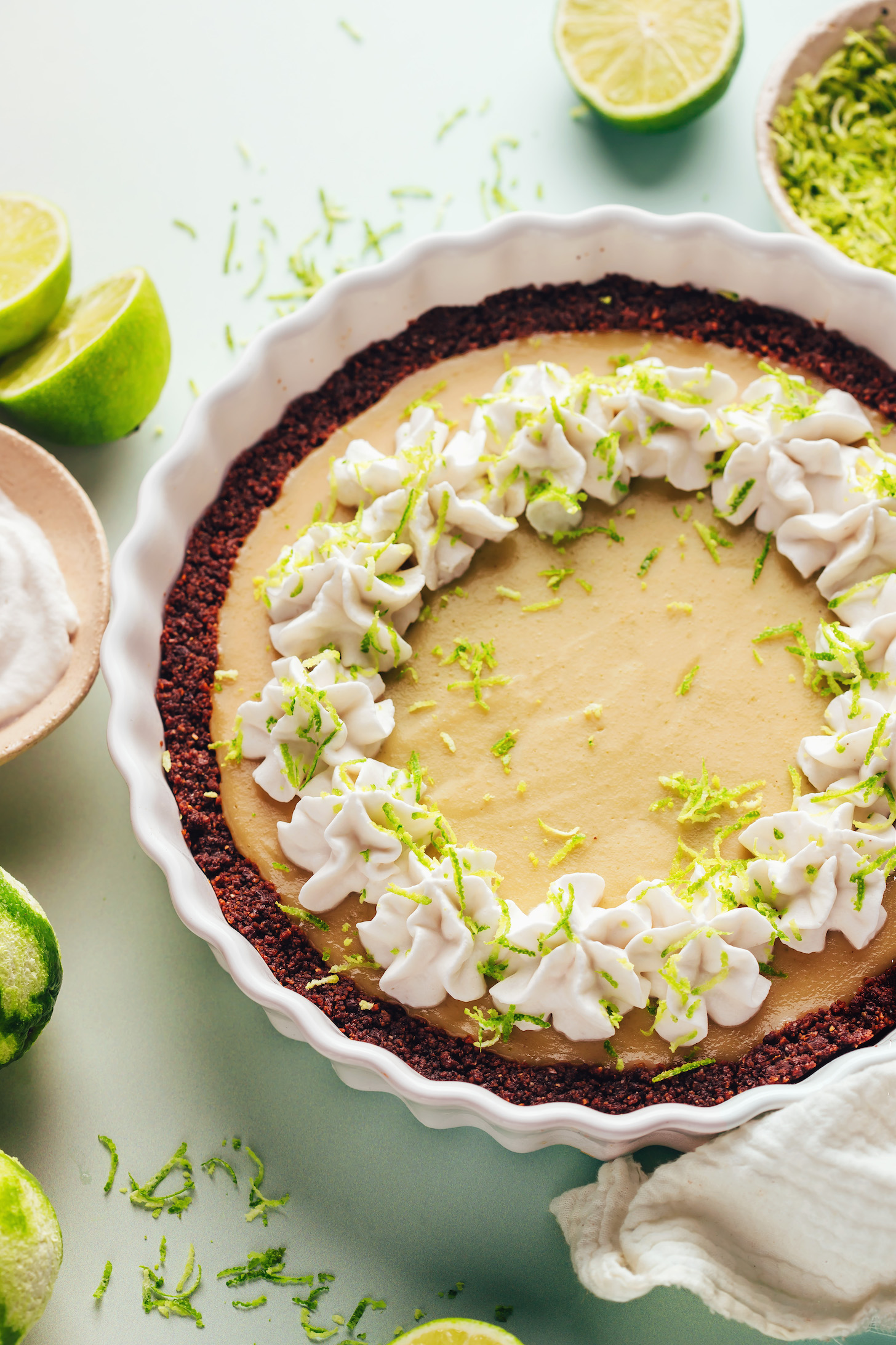 Limes and cashew whipped cream next to a pie plate filled with vegan key lime pie