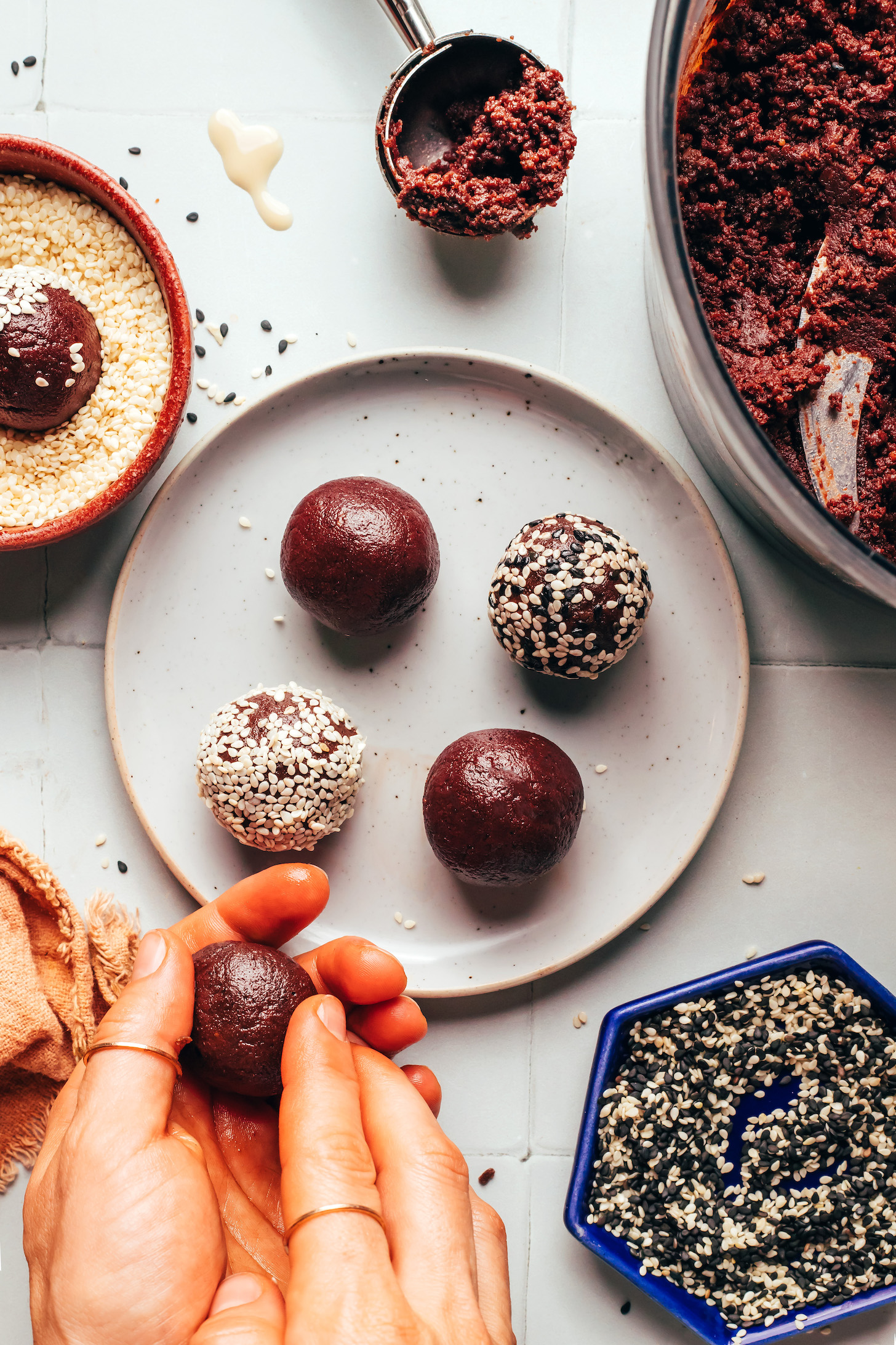Rolling a chocolate tahini truffle next to a plate with more truffles