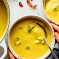 Overhead shot of hands holding the sides of a bowl of creamy vegan broccoli cheddar soup