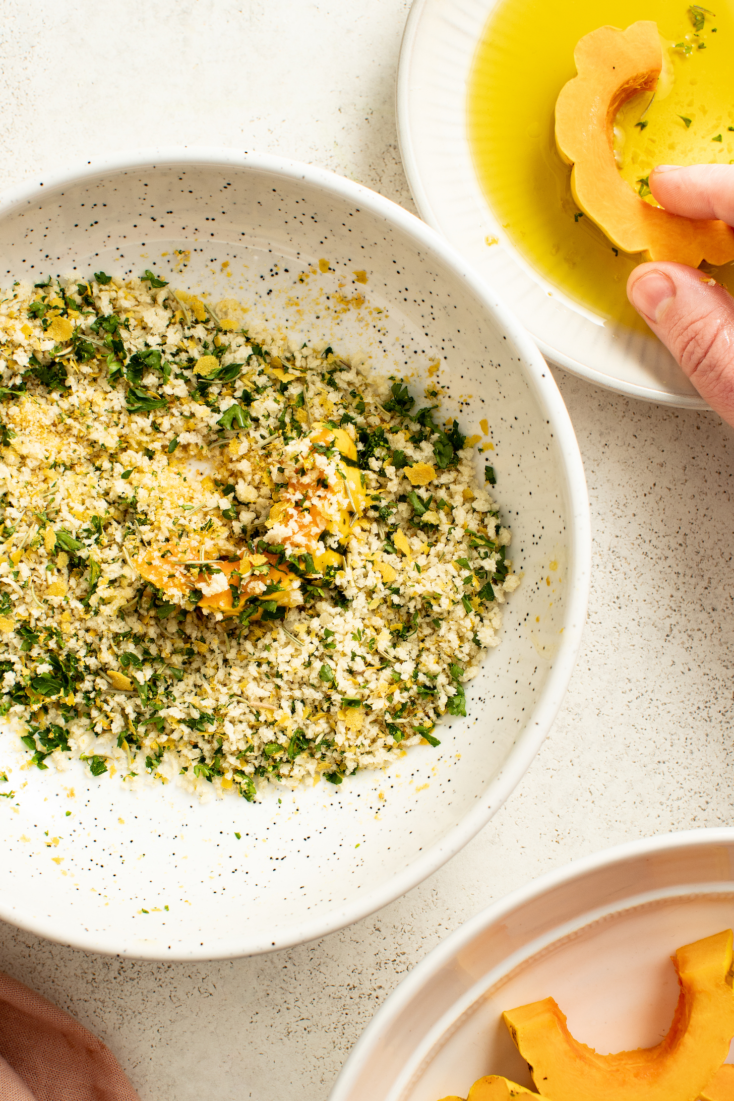 Dipping a slice of squash into a bowl of olive oil next to a bowl of garlic & herb breading