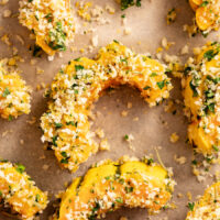 Close up photo of garlic & herb breaded delicata squash on a parchment-lined baking sheet