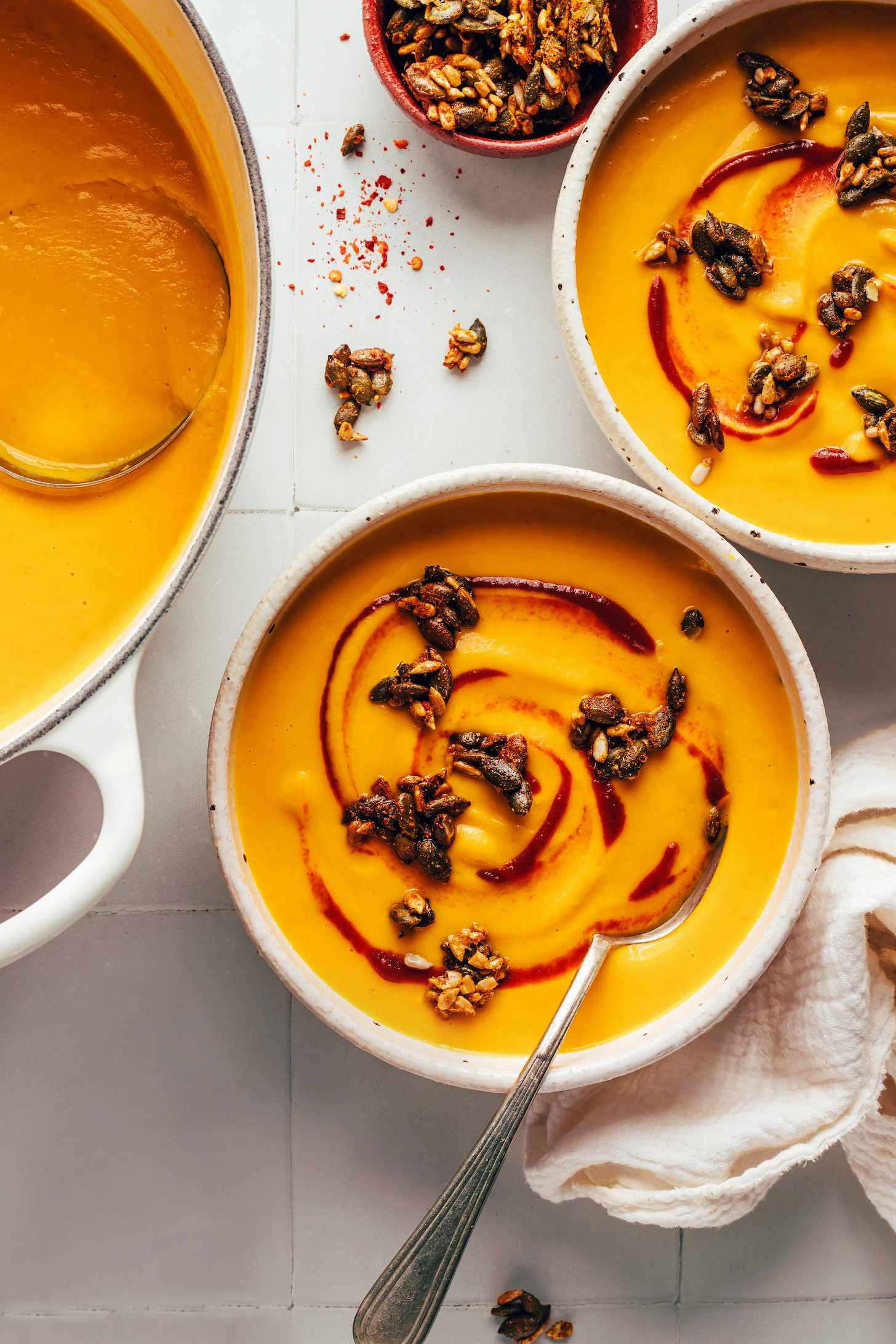 Two bowls and a large pot of creamy carrot ginger soup