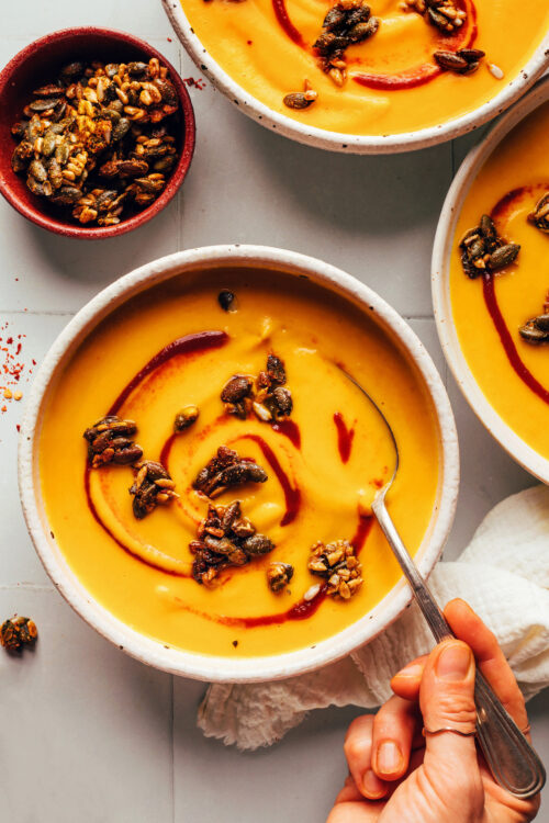 Holding a spoon in a bowl of creamy vegan carrot ginger soup