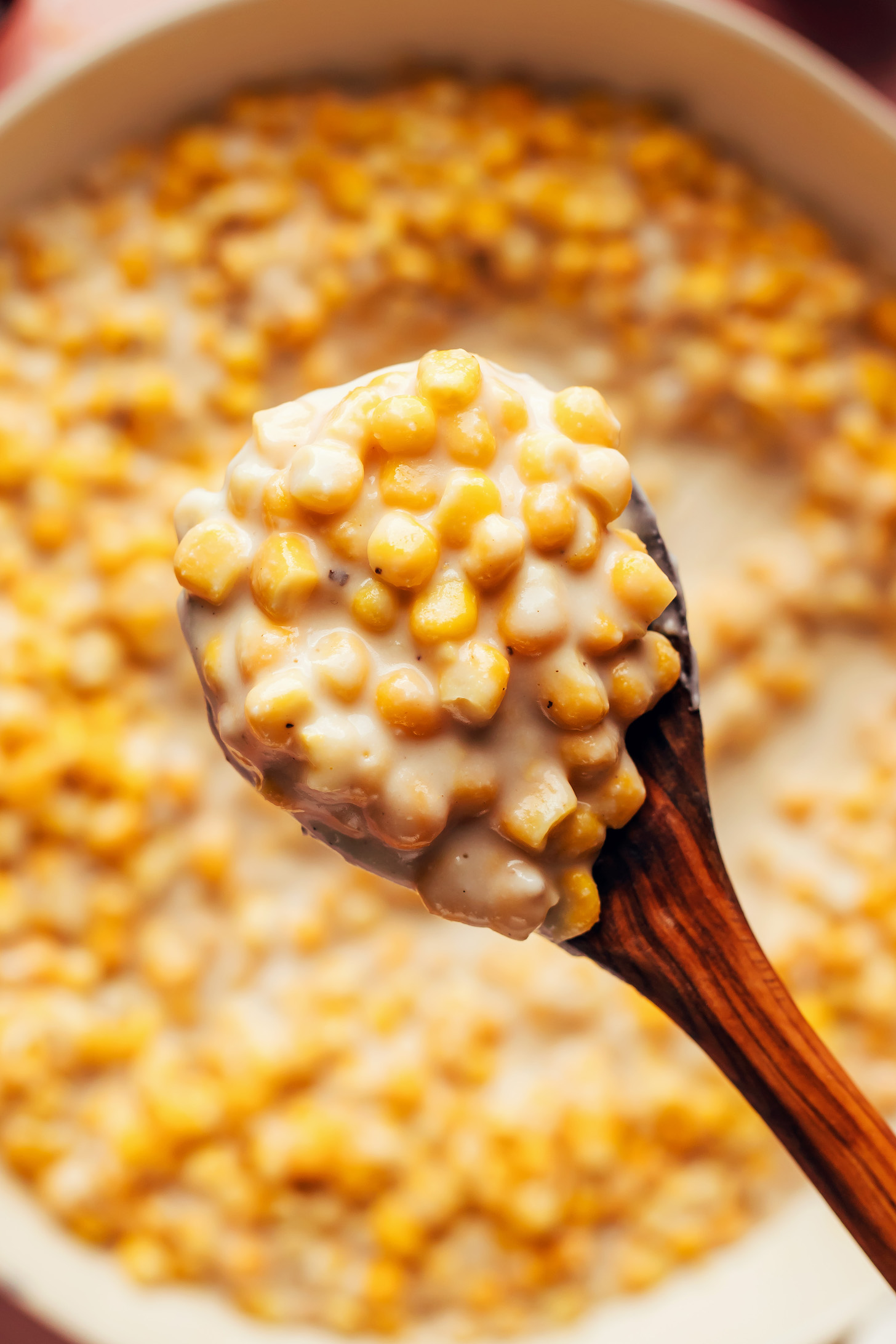 Holding a serving spoon filled with vegan creamed corn over a pan with more of it