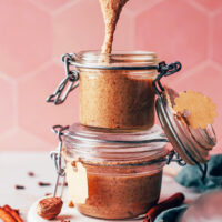 Chai-spiced cashew almond butter falling off a spoon into a jar stacked on another jar of nut butter