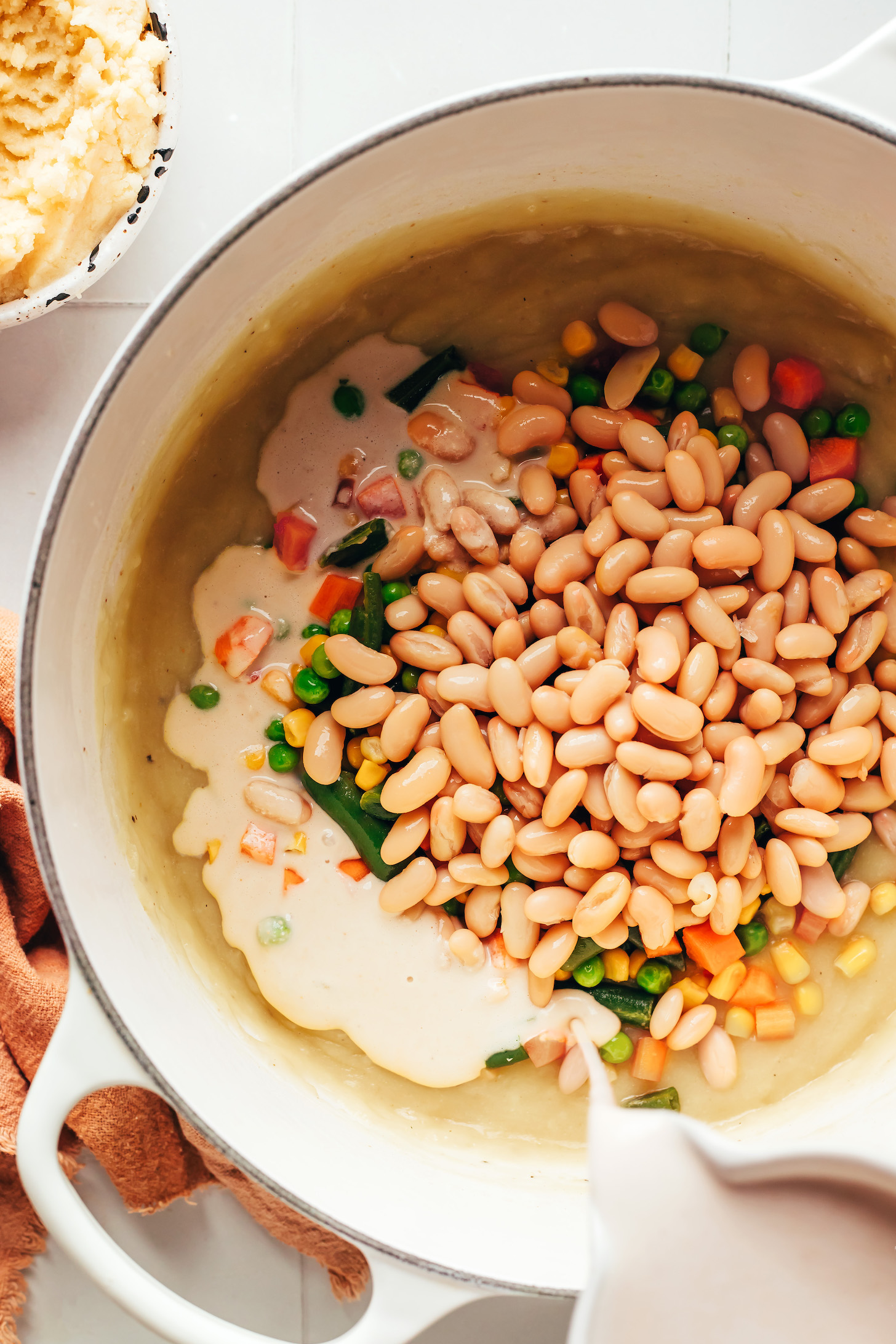 Pouring creamy cashew milk over mixed vegetables and white beans