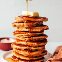 Pouring maple syrup onto a stack of homemade gluten-free pancakes
