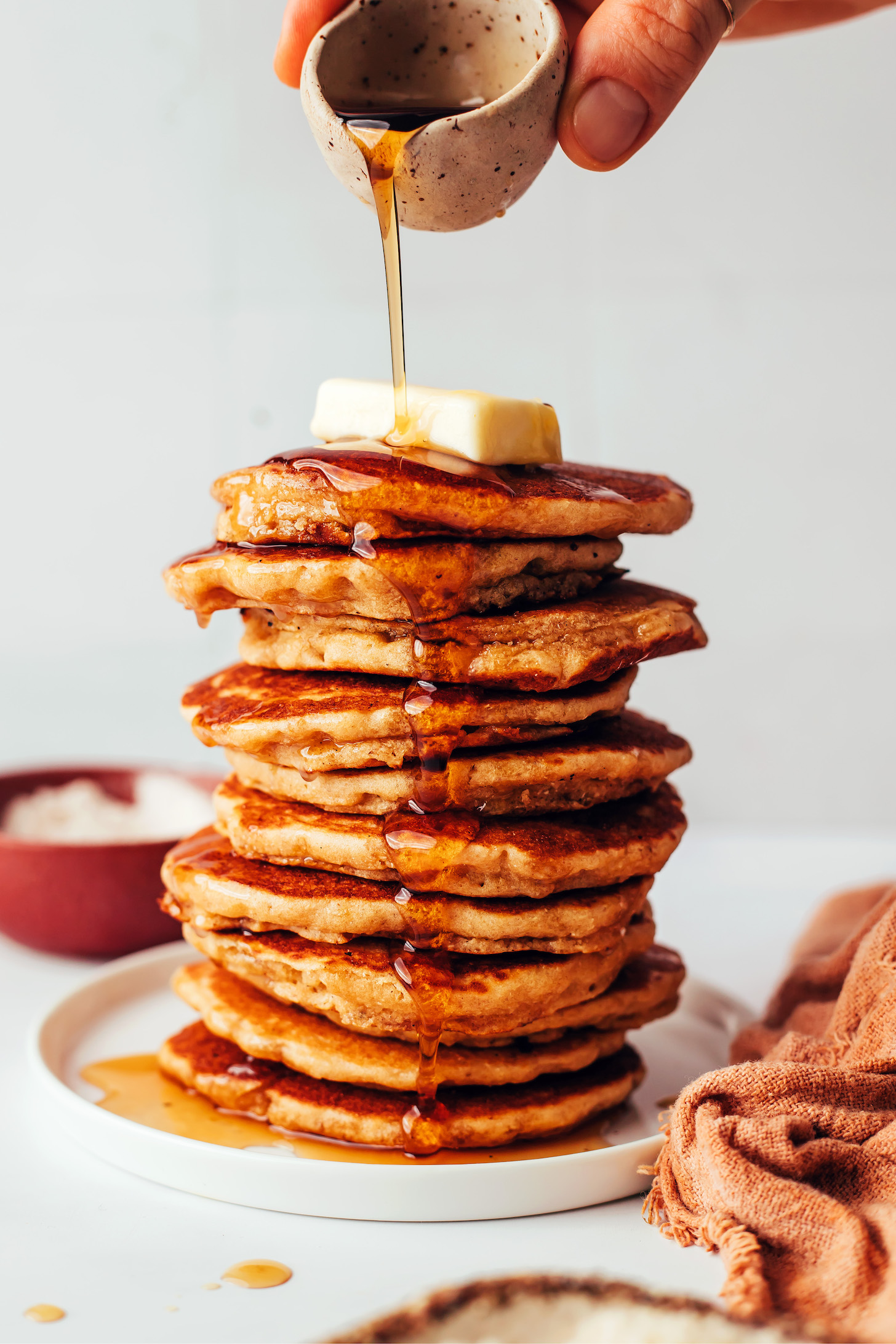 Pouring maple syrup onto a stack of fluffy gluten-free pancakes