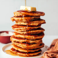 Pouring maple syrup onto a stack of fluffy gluten-free dairy-free pancakes