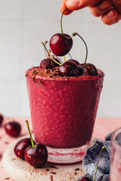 Placing a fresh cherry on the top of a chocolate cherry protein smoothie