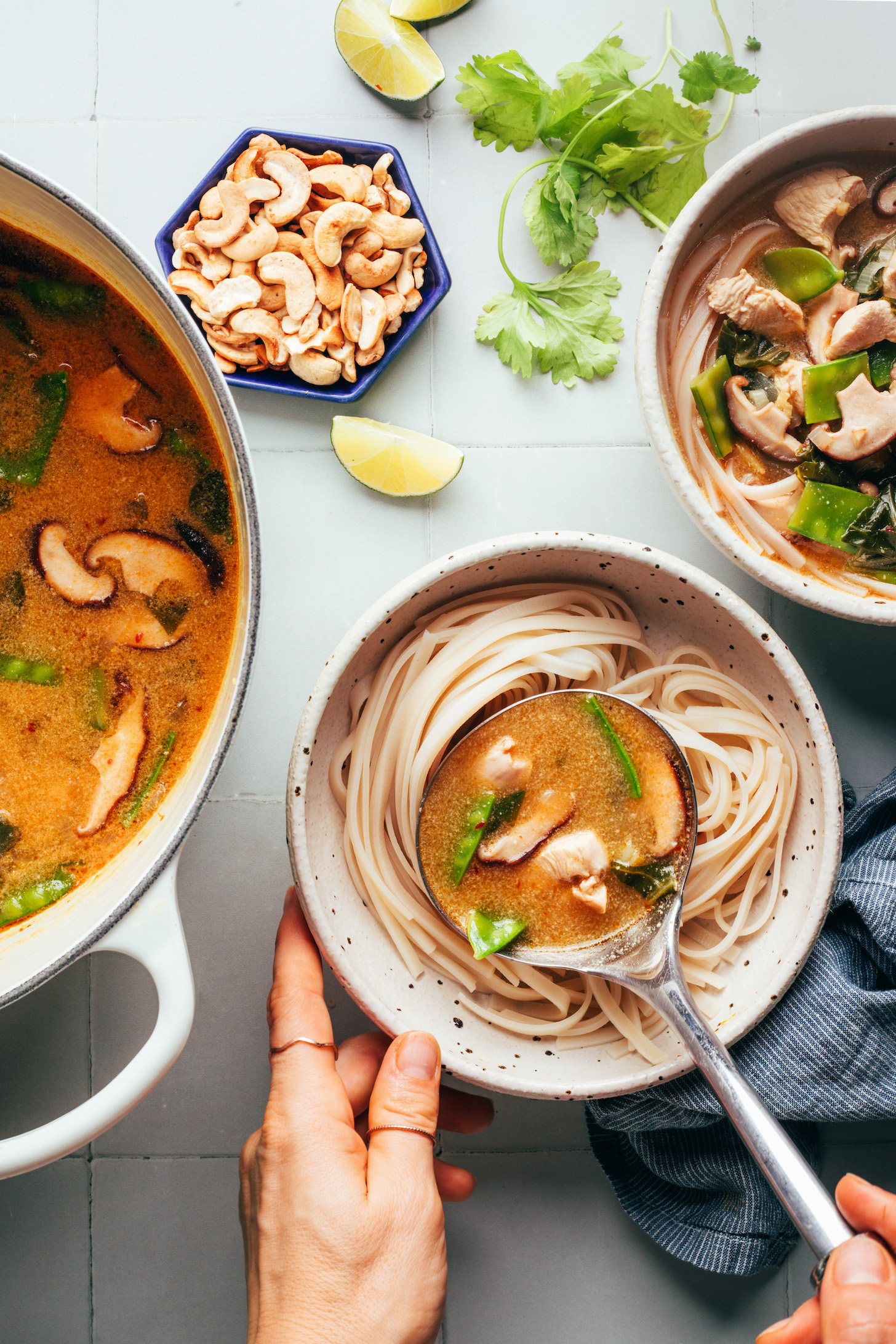 Using a ladle to add a cozy curry broth with chicken and veggies to a bowl of cooked brown rice noodles