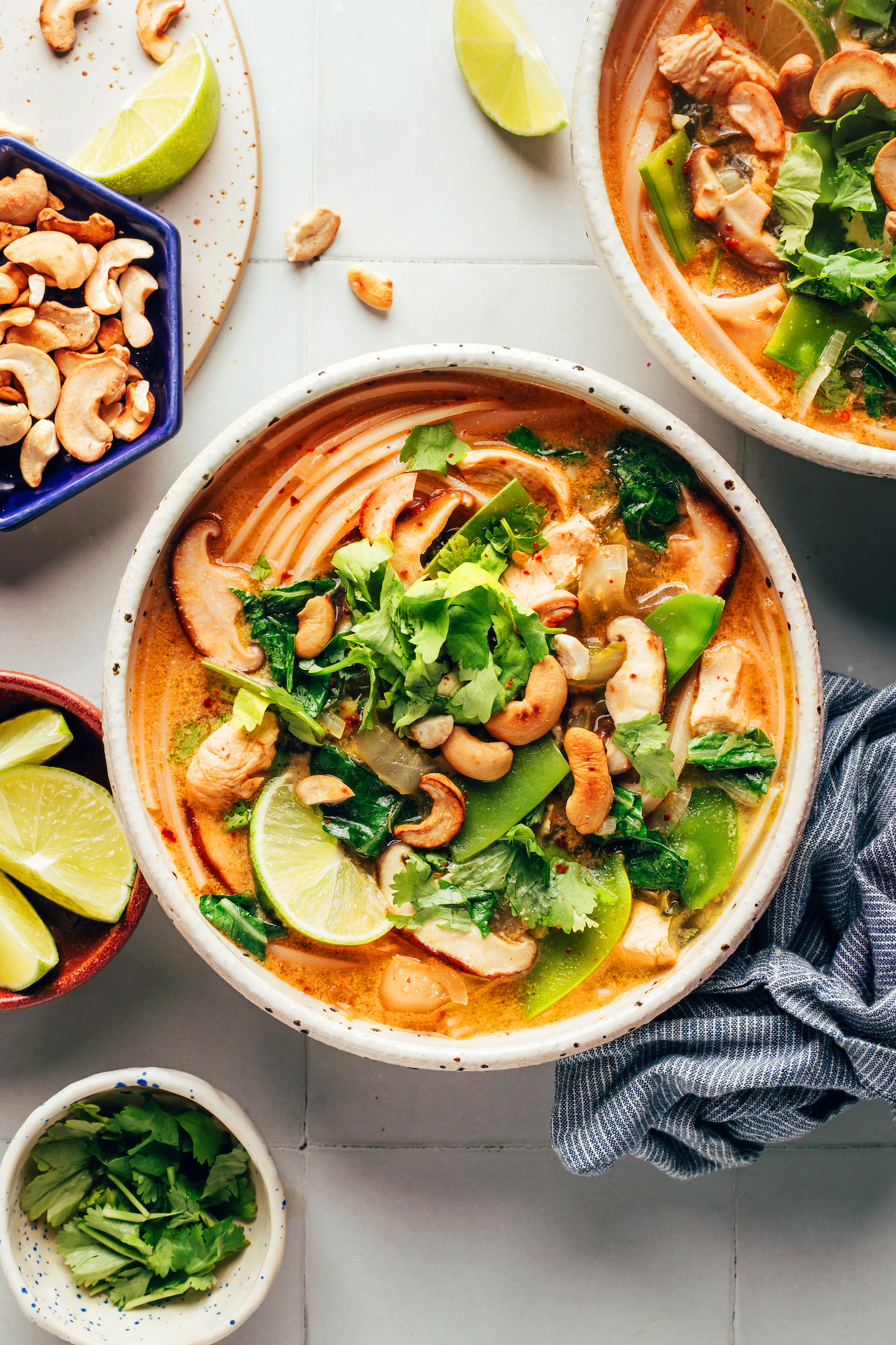 Two bowls of our cozy curry noodle soup topped with cashews, cilantro, and lime wedges