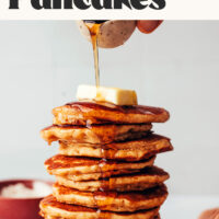 Pouring maple syrup onto a stack of gluten-free pancakes