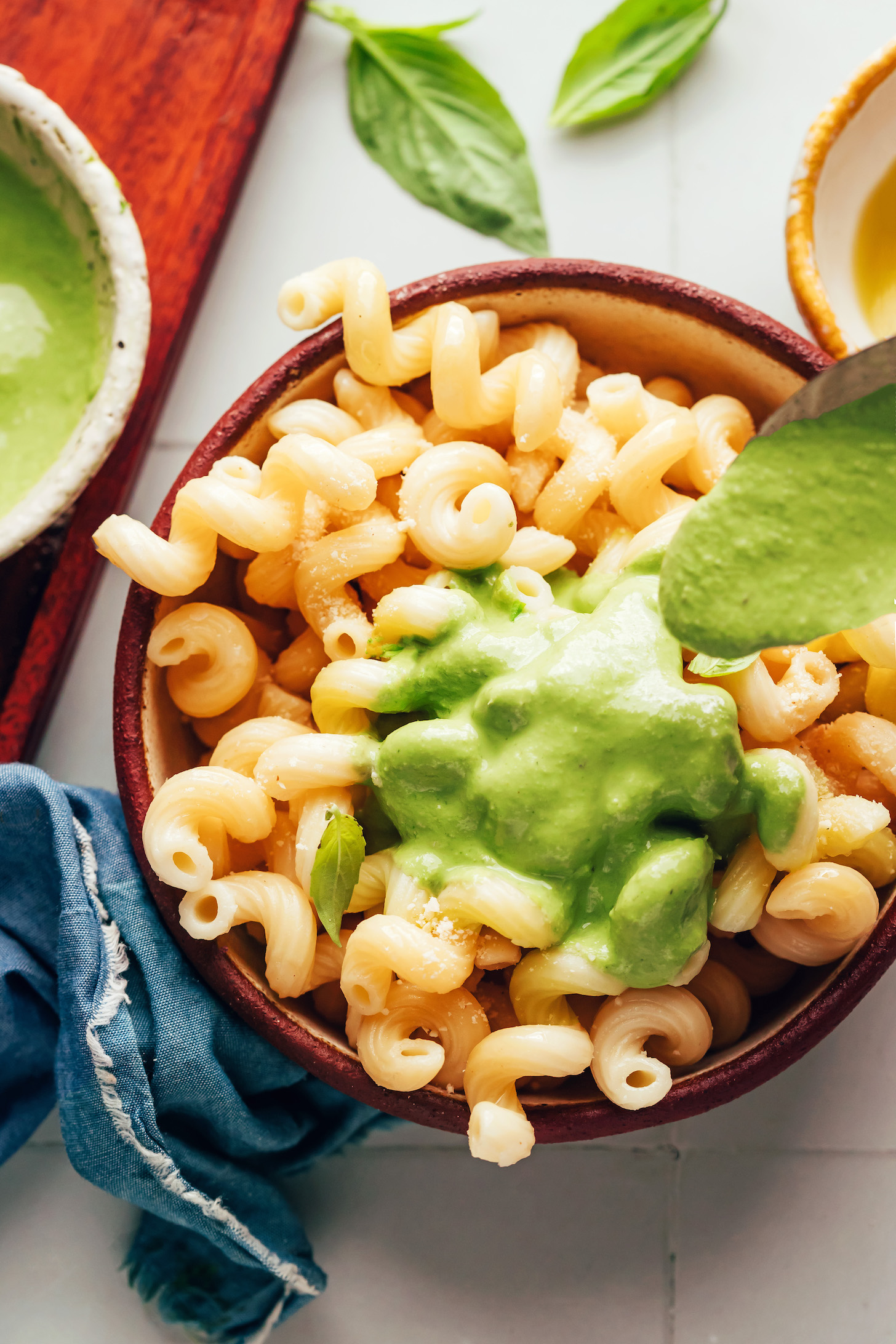 Drizzling a dairy-free creamy pesto sauce over a bowl of cooked pasta