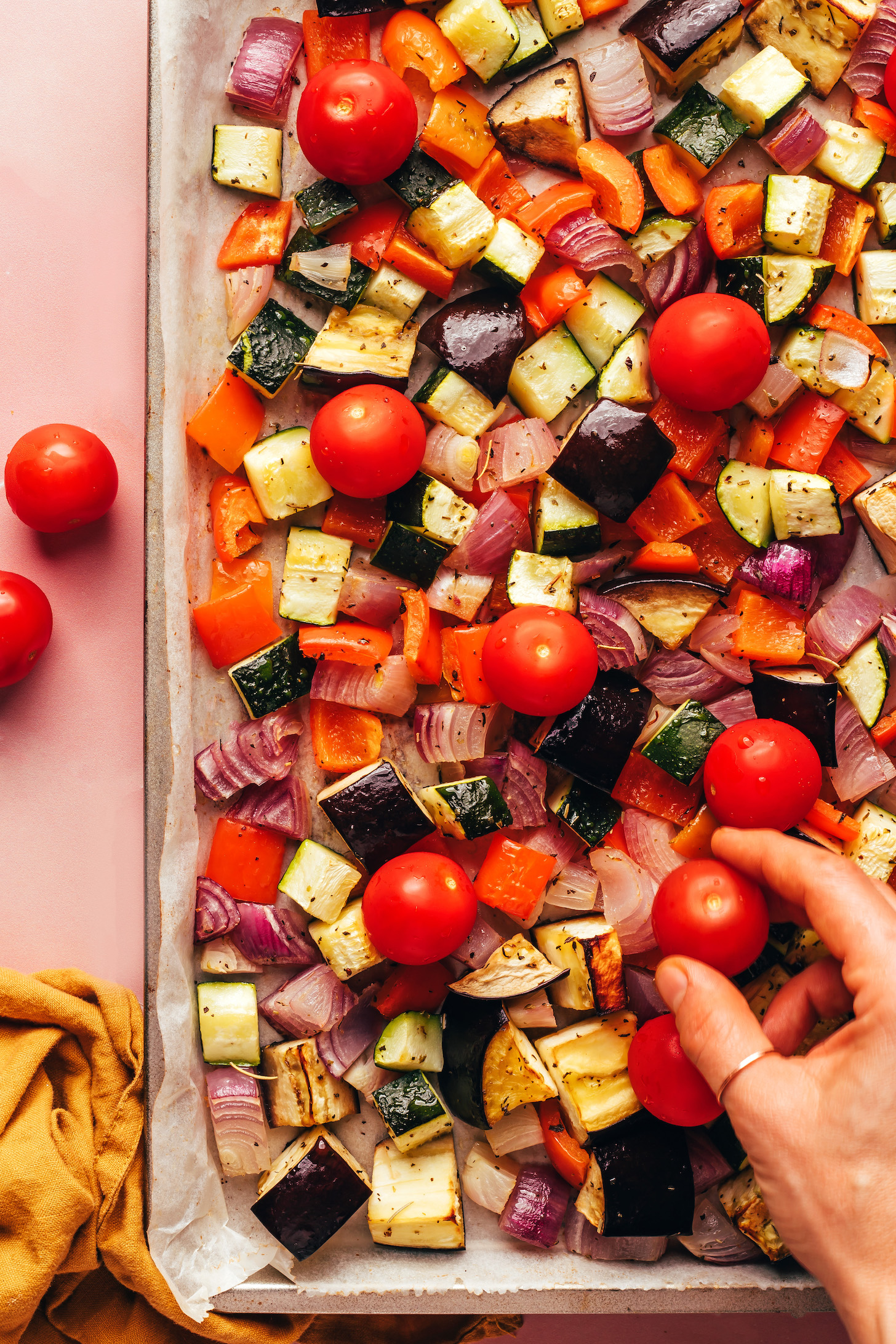 Placing tomatoes onto a baking sheet of partially roasted ratatouille vegetables