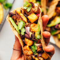 Holding up a vegan jerk cauliflower taco topped with avocado and mango hot sauce