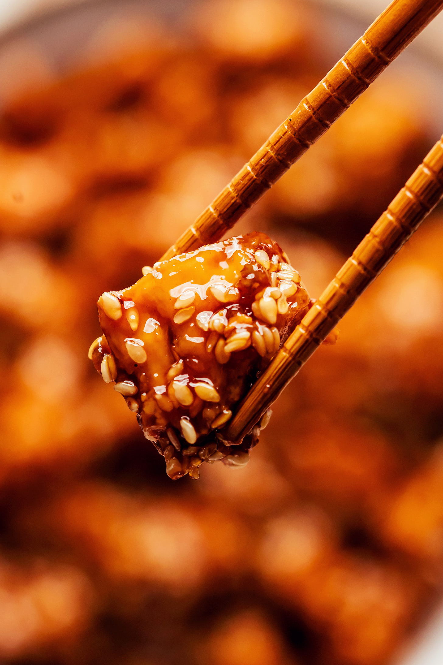 Close up shot of chopsticks holding a bite of vegan sesame tofu