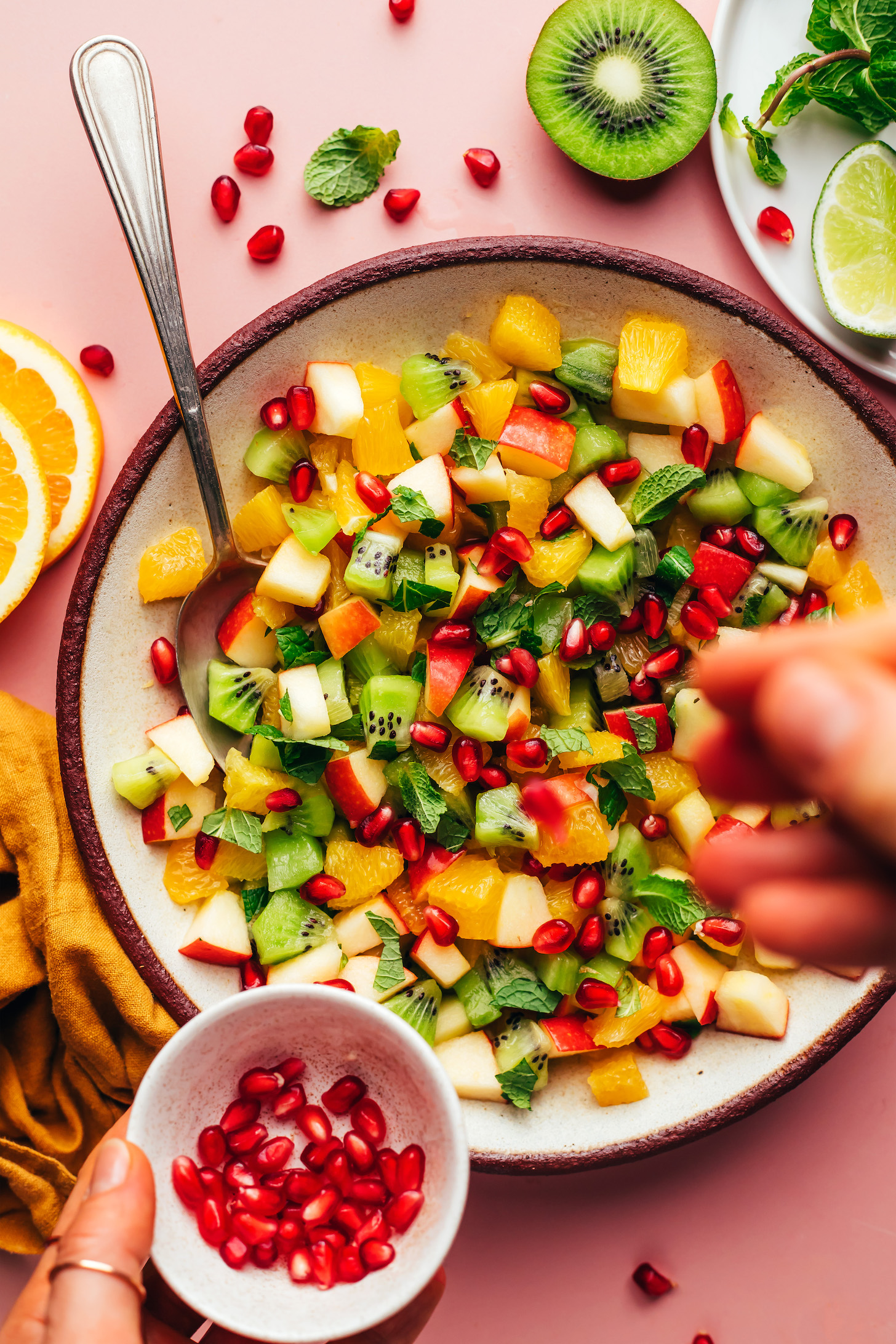 Sprinkling pomegranate arils into a bowl of our easy winter fruit salad