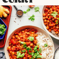 Two bowls of our warming 1-pot vindaloo-inspired chickpea curry served with rice and cilantro