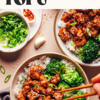Text reading Spicy Garlicky Sesame Tofu ready in 30 minutes written above a bowl of sesame tofu with rice and broccoli