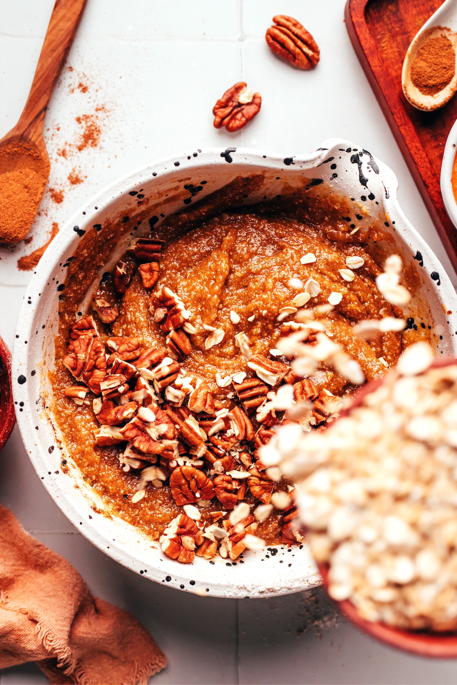 Adding rolled oats to a bowl of cookie dough with chopped pecans on top