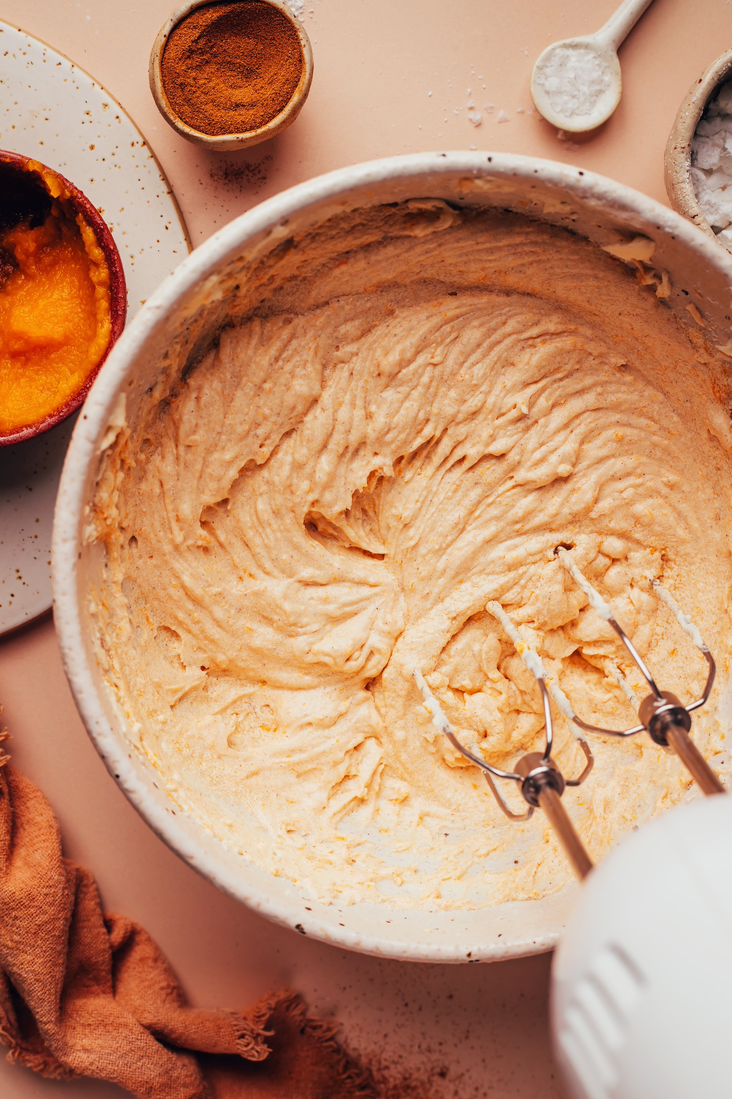 Using an electric mixer in a bowl of vegan pumpkin spice frosting