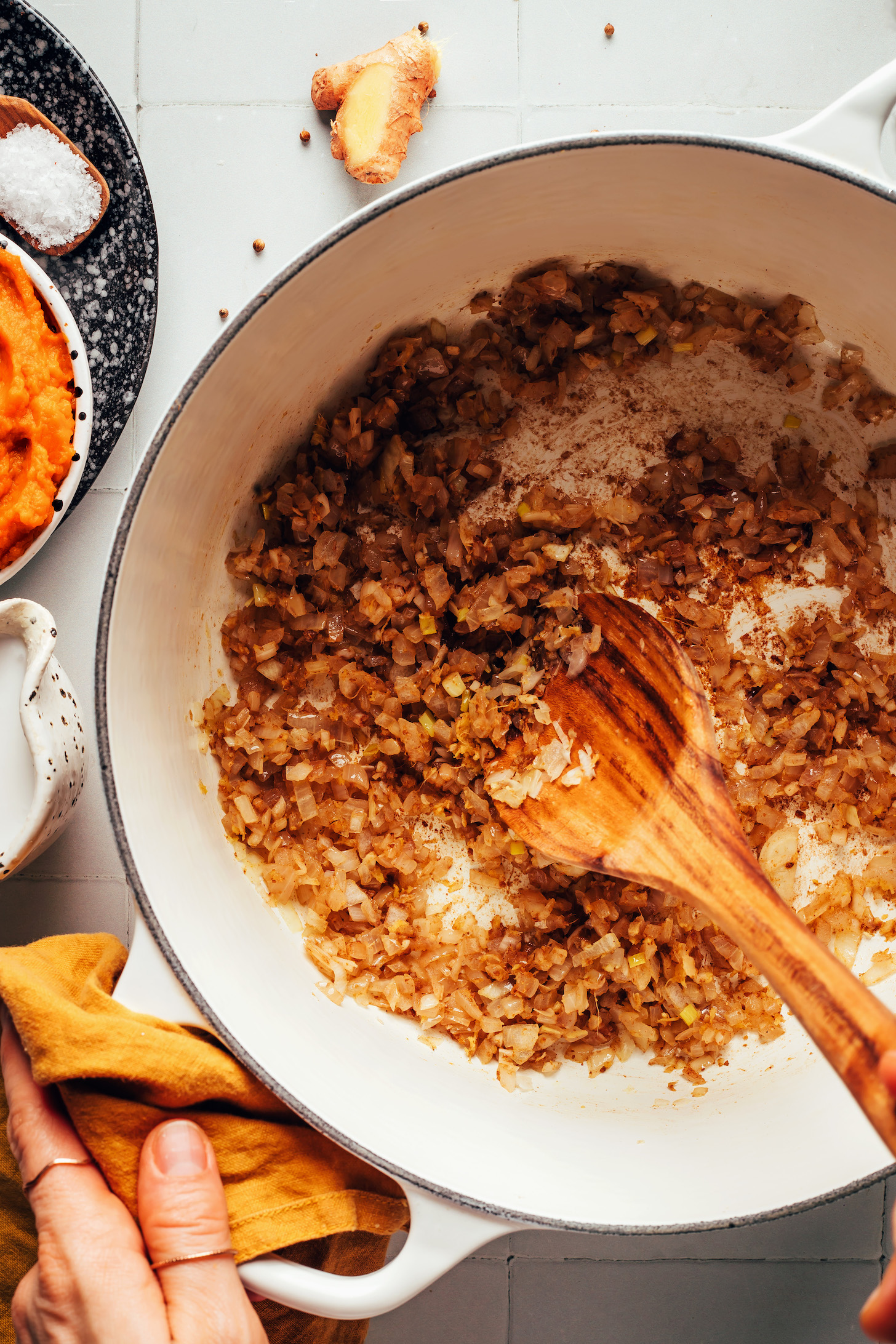 Using a wooden spoon to stir sautéed onion, garlic, and ginger with dried spices