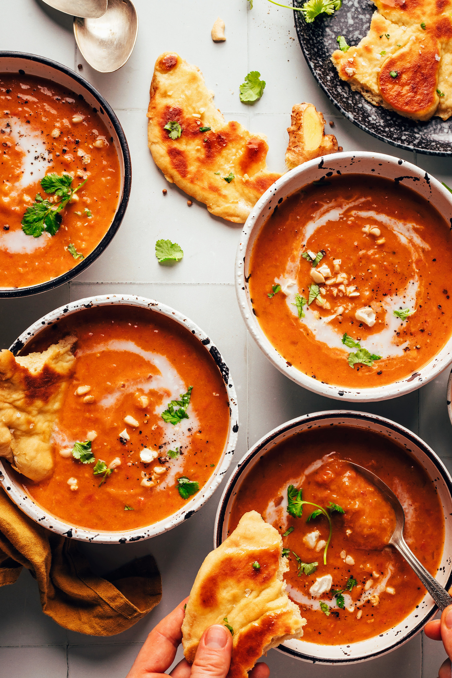 Bowls of spicy pumpkin tomato soup topped with coconut milk, cashews, and cilantro and served with naan