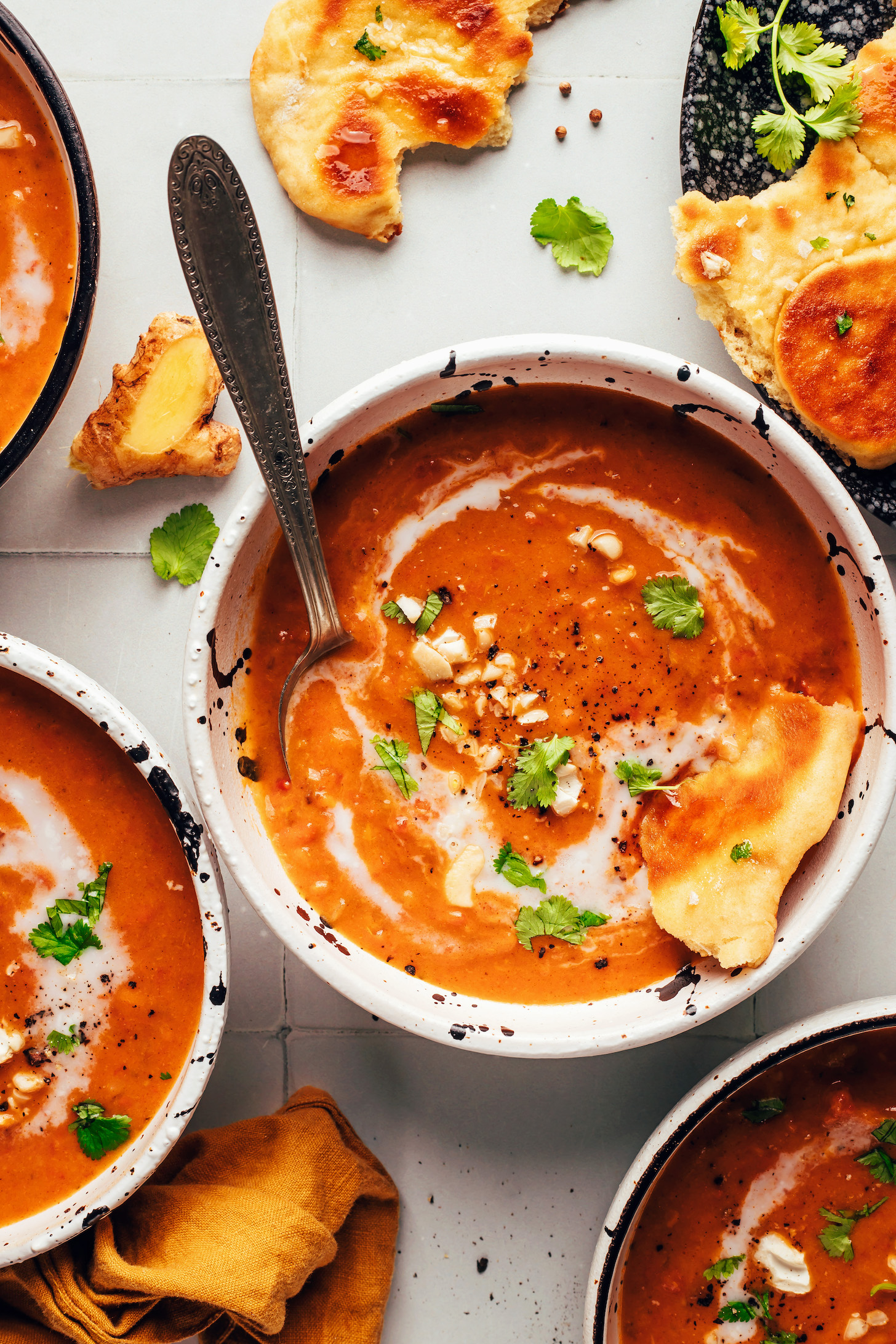 Bowls of spicy pumpkin tomato soup topped with coconut milk, cashews, cilantro, and naan