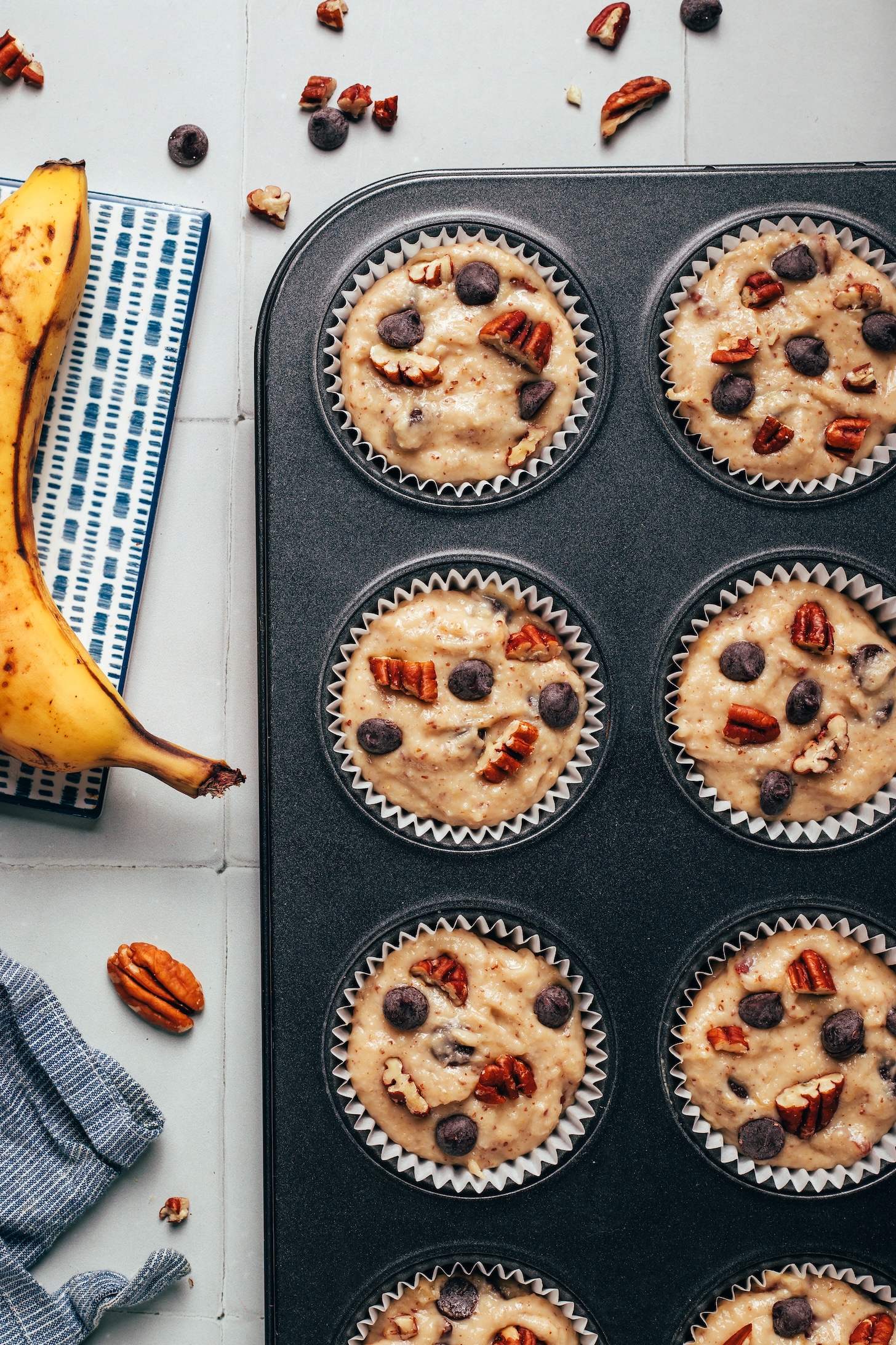 Overhead photo of a muffin tin filled with batter and topped with extra chocolate chips and pecans