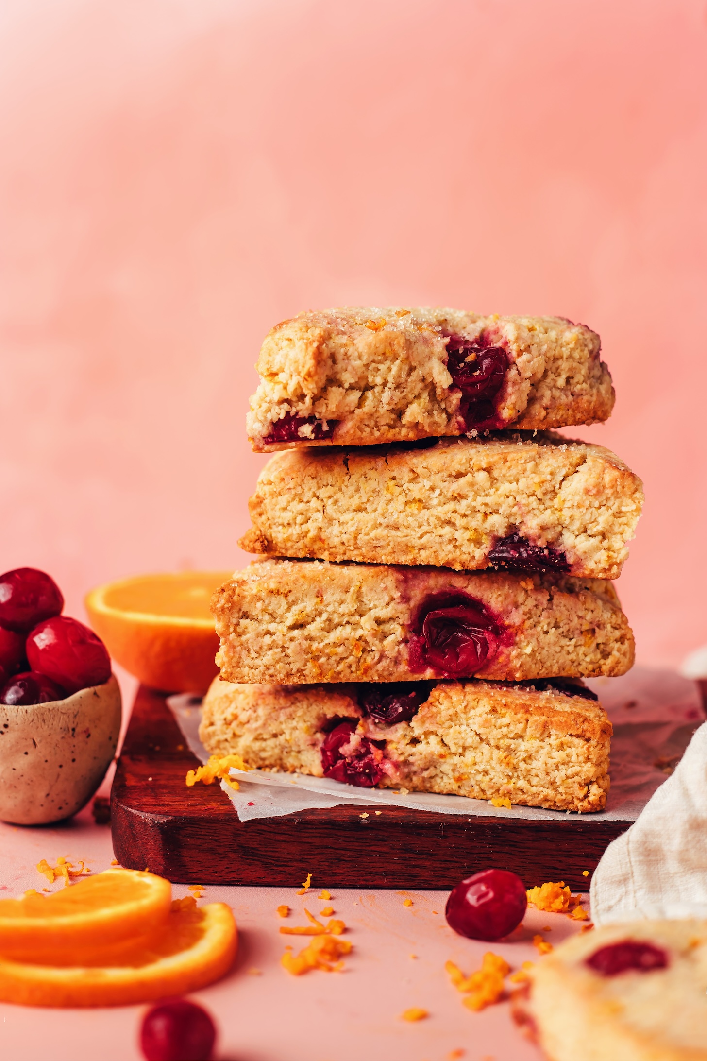 Stack of vegan gluten-free cranberry orange scones next to orange slices and cranberries