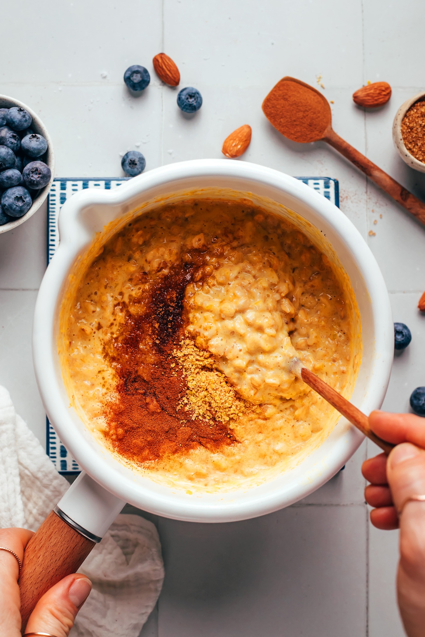 Stirring creamy pumpkin oats with spices and brown sugar in a small white saucepan