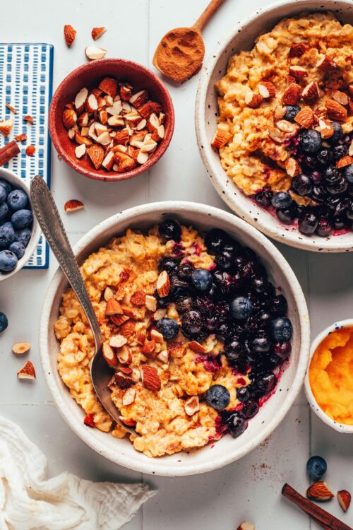 Two bowls of our creamy pumpkin oats topped with blueberries and toasted almonds