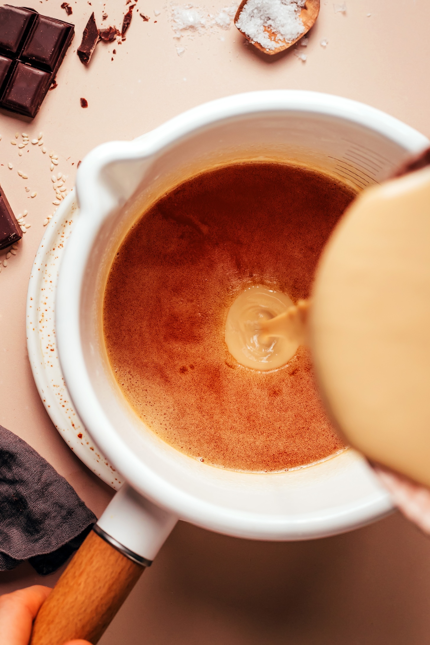 Pouring tahini into a saucepan of a caramelized vegan butter and maple syrup mixture