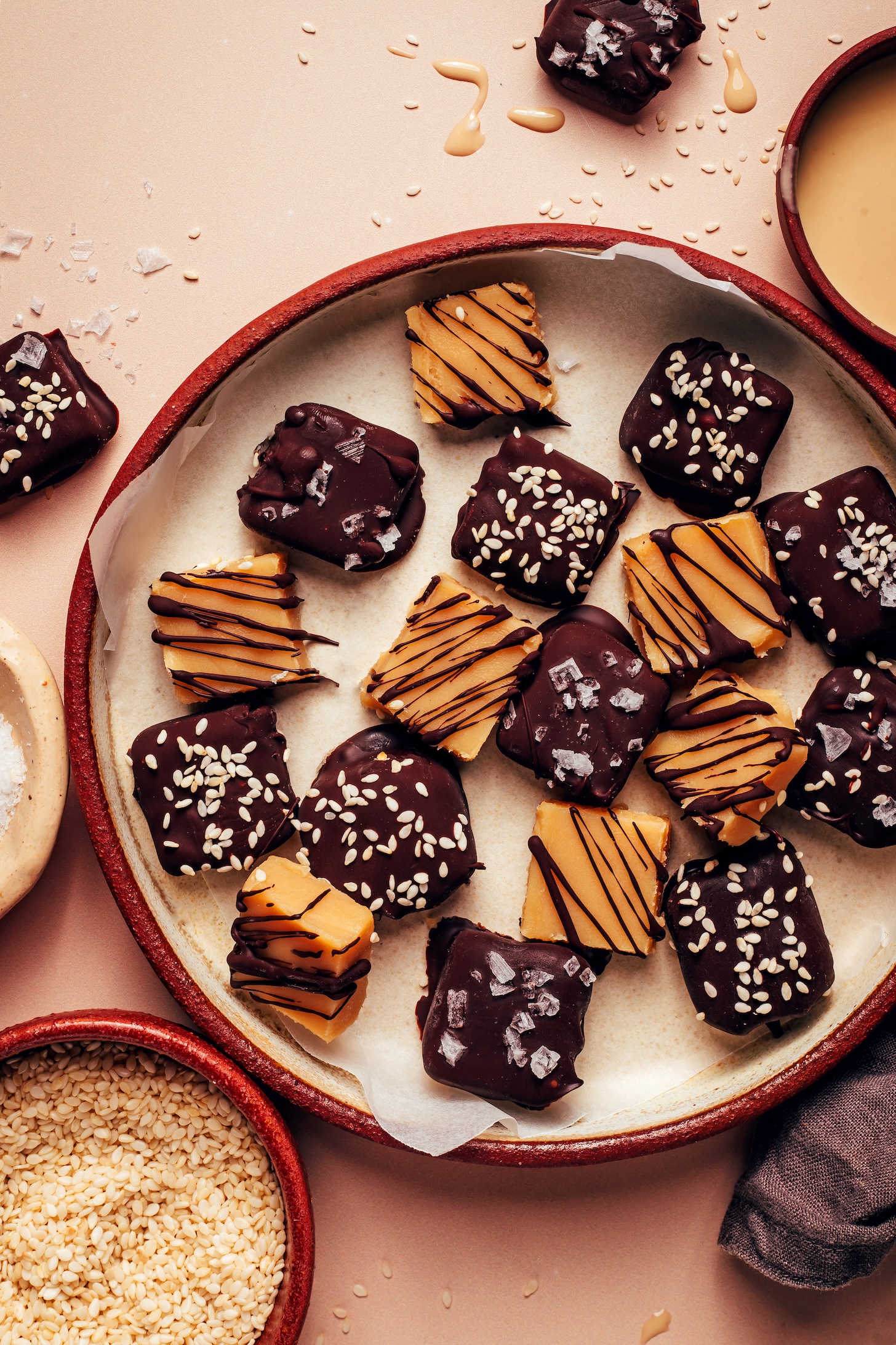 Plate of sea salt tahini caramels with some drizzled and others dunked in dark chocolate with sea salt and sesame seeds