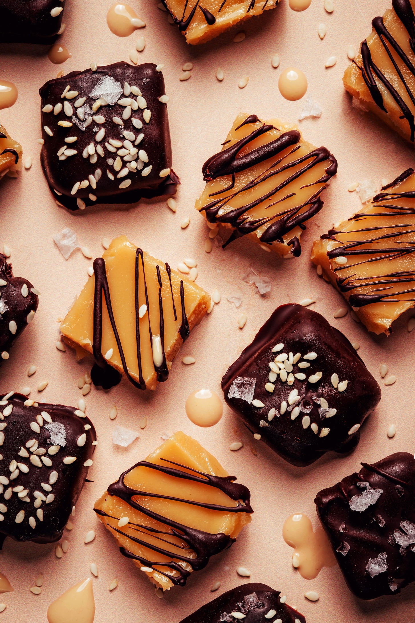 Overhead photo of vegan sea salt tahini caramels with some drizzled with chocolate and others with a chocolate coating, flaky salt, and sesame seeds