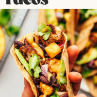 Hand holding a taco with text above it reading Jerk Cauliflower Tacos with Mango Hot Sauce