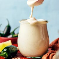 Vegan cashew jalapeño dressing dripping off a spoon into a small glass jar