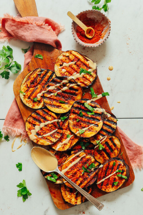 Grilled eggplant slices on a wood cutting board with a spoonful of tahini