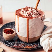 Overflowing mug of our vegan tahini hot chocolate topped with coconut whipped cream and shaved dark chocolate