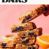 Picking up a cookie bar from a stack of vegan gluten-free cranberry orange cookie bars