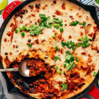 Spoon resting in a pan of our cheesy vegan enchilada skillet recipe