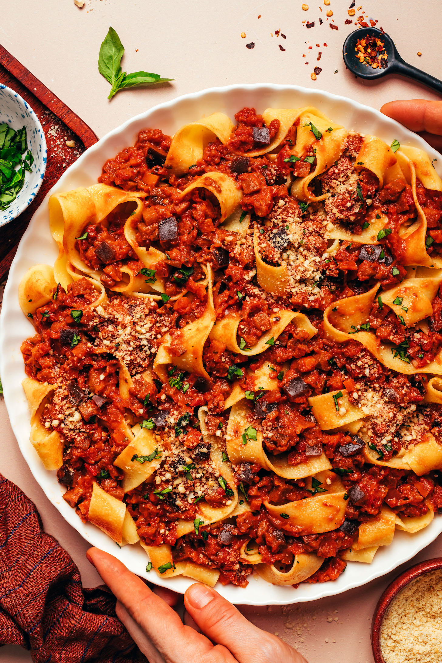 Hands holding the sides of a large plate of our eggplant bolognese served with pappardelle